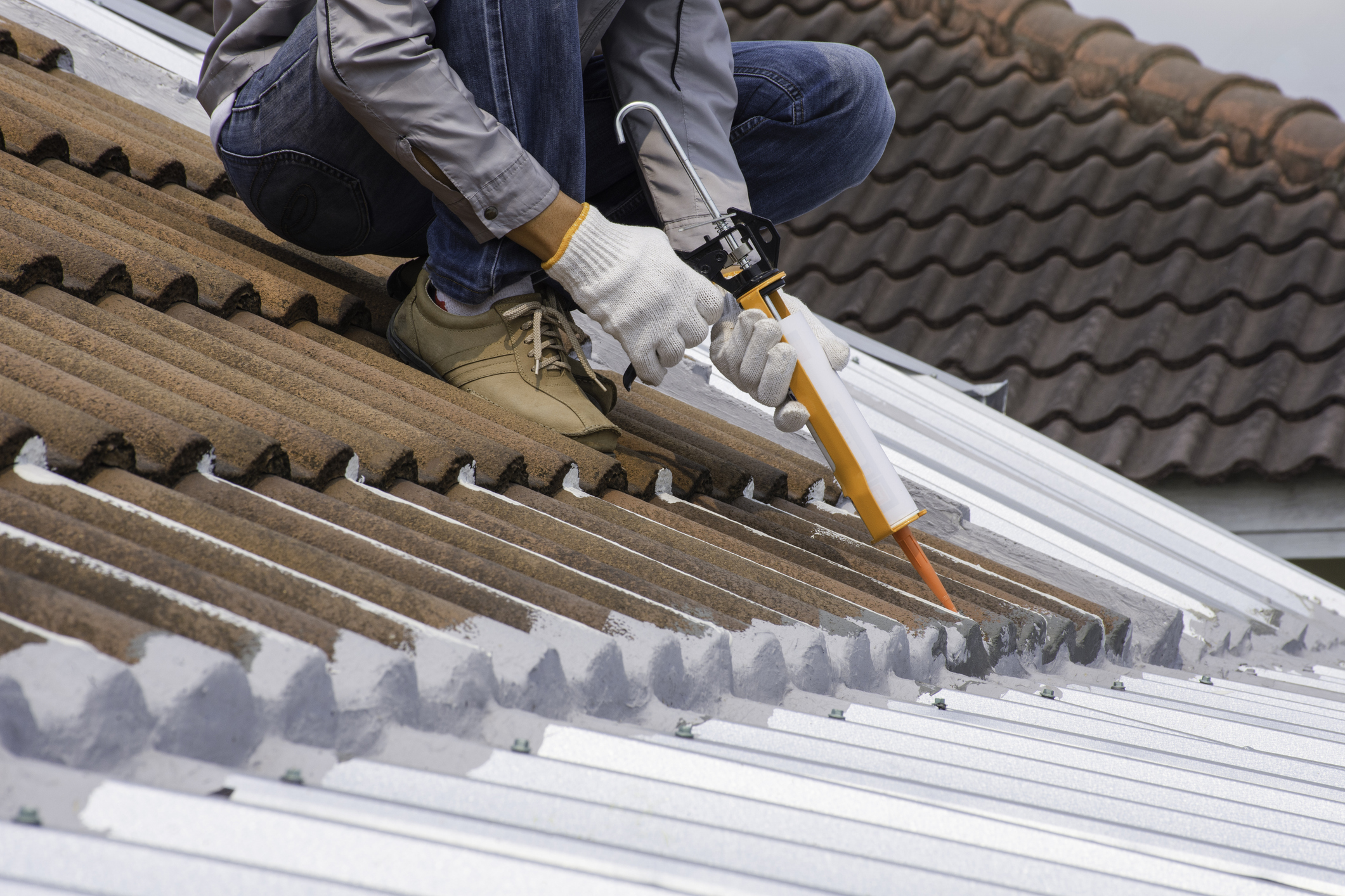 A man is working on a roof, using a metal tool to perform repairs or maintenance.