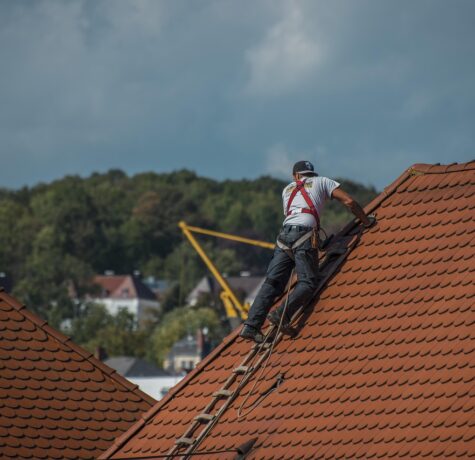A man on a ladder performing roofing repair on the roof of a house.
