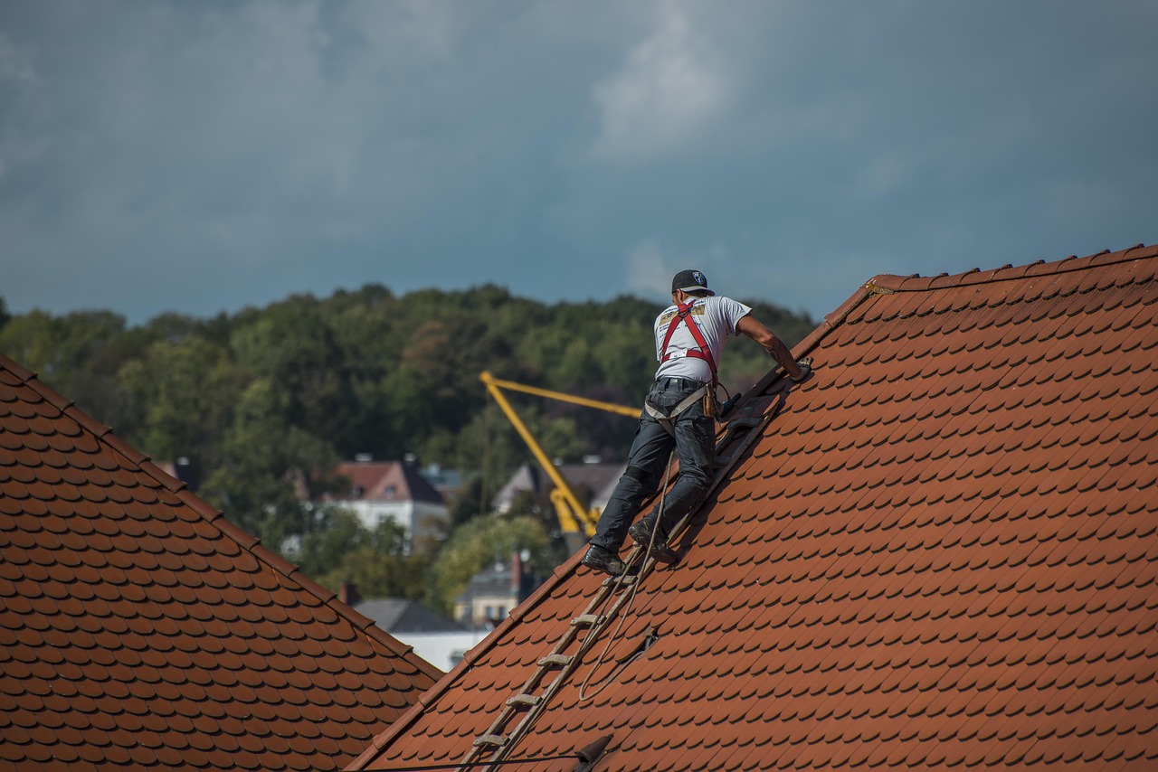 A man on a ladder performing roofing repair on the roof of a house.