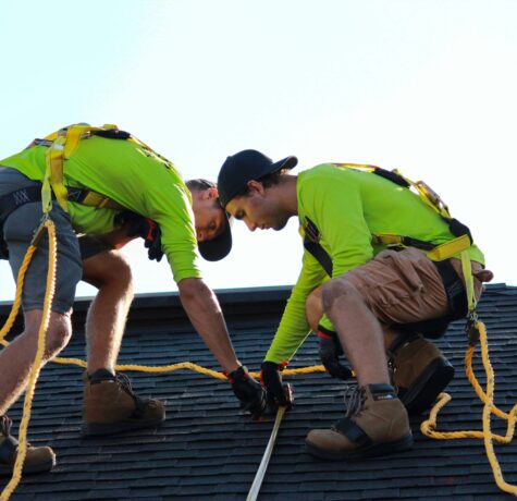 Two men in green shirts working on a roof, focused on restoration tasks in Sydney.